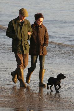 a man and woman walking on the beach with a dog