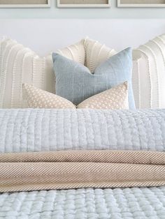 a bed with pillows and blankets on top of it in front of three framed pictures