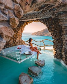 a woman sitting on a bed in the middle of a body of water with rocks around her