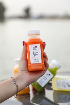 a woman holding up a bottle of orange juice on top of a table next to other bottles