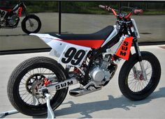 a red and white dirt bike parked in front of a glass building with the number 99 on it