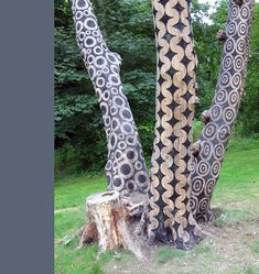 the trunk of a tree with intricate designs on it's bark, in front of some green grass and trees