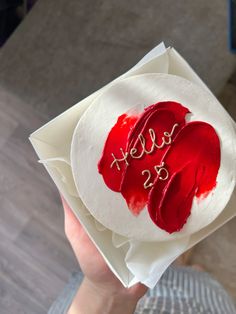 a person holding up a cake with red icing on it