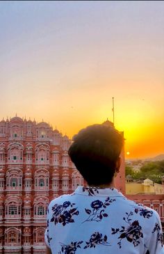 a person standing in front of a pink building with the sun setting on it's side