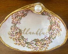 a decorative dish with the word thank written in gold lettering on it and a pearl bead