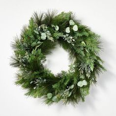 a green wreath with white flowers and greenery hanging on the wall in front of a white wall