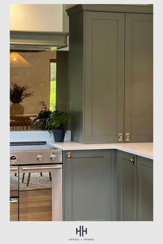 an image of a kitchen setting with green cabinets and white counter tops, along with a potted plant in the corner