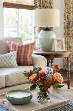 a living room filled with furniture and flowers on top of a coffee table in front of a window