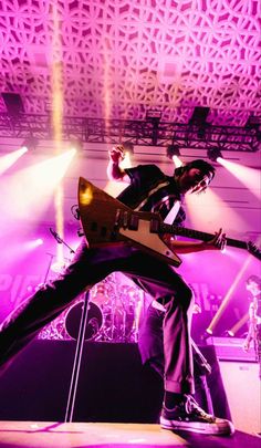 a man on stage with his guitar in the air and purple lighting behind him,