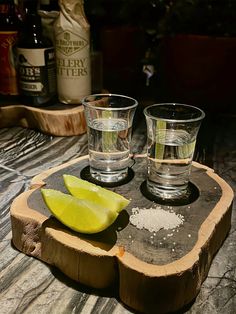 two shot glasses sitting on top of a wooden tray next to a slice of lemon