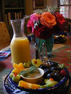 a blue plate topped with fruit and vegetables next to a vase filled with orange juice