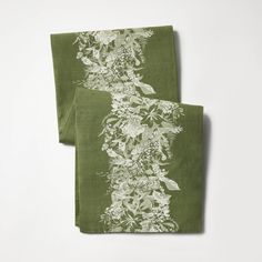 two green napkins with white flowers and leaves on them, one is folded to the side