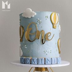 a blue cake with gold lettering and hot air balloons on top that says one above it