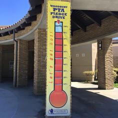 a tall yellow and red thermometer sitting in front of a building