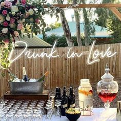 a table with wine glasses and bottles on it in front of a wooden fence that says drunk in love