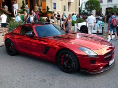 a red sports car parked in front of a building with people walking around it and onlookers