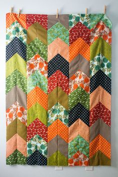 a quilt hanging on the wall with clothes pins in front of it and an orange, green