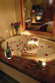 a bathtub with rose petals on the floor next to a mirror and bottle of champagne