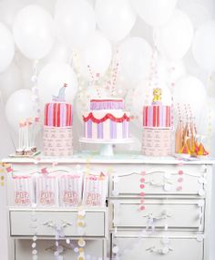 a table topped with lots of cakes and balloons in front of a white wall filled with confetti