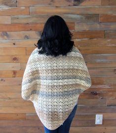 a woman standing in front of a wooden wall wearing a white and black knitted sweater