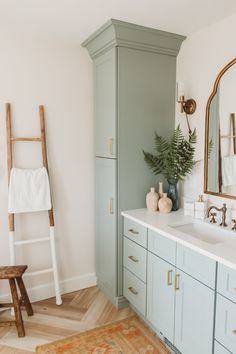 a bathroom with blue cabinets and white counter tops, gold accents and a ladder leaning against the wall