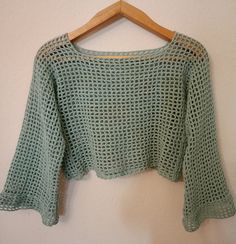 a green crocheted sweater hanging on a wooden hanger next to a white wall