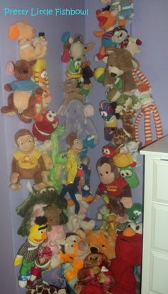 there are many stuffed animals in the corner of this room, and one is hanging on the wall