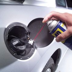 a man is opening the fuel cap on his car and spraying it with a spray