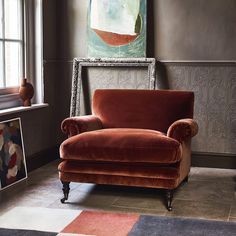 an orange velvet chair sitting in front of a window with a painting on the wall