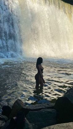 a woman standing in the water next to a waterfall