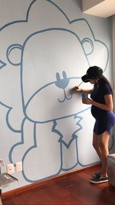 a woman is painting a wall with a teddy bear design on it and wearing a blindfold