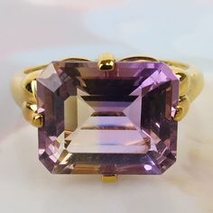 "A mesmerizing golden purple 5.4 carat ametrine gemstone tops this vintage 1970s 10k yellow gold ring. Rarely found in nature, Ametrine is a quartz crystal with the presence of both amethyst and citrine. This bi-color quartz gem has 60/40 split zones of purple amethyst and yellow citrine. The 12.1mm x 10mm x 6.5mm faceted ametrine has nice translucency and clarity.  Four sturdy prongs hold the gem above an airy raised setting. The ring is finished with flanking rounded petal shapes on the should Luxury Gold Emerald Cut Amethyst Ring, Yellow Gold Emerald-cut Amethyst Ring For Formal Occasions, Gold Amethyst Ring Collectible Fine Jewelry, Gold Amethyst Ring Fine Jewelry Collectible, Gold Amethyst Ring, Fine Jewelry Collectible, Gold Amethyst Ring In Fine Jewelry Style, Gold Amethyst Ring For Collectors, Art Deco Amethyst Ring In Yellow Gold, Yellow Gold Amethyst Ring In Art Deco Style