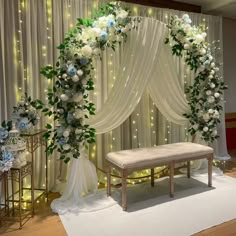 a white and blue wedding ceremony setup with flowers on the wall, draped drapes and bench