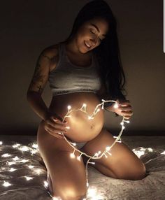 a pregnant woman sitting on top of a bed with fairy lights around her stomach and belly