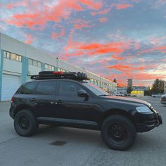 a black suv parked in front of a building under a cloudy sky with pink clouds