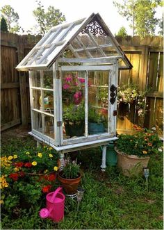 a small greenhouse in the middle of a yard with flowers and potted plants around it