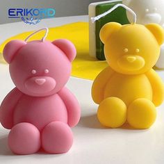 two small plastic teddy bears sitting next to each other on a white table with yellow and pink decorations