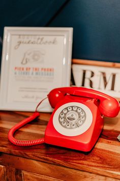 an old red telephone sitting on top of a wooden table next to a framed photo