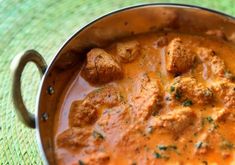 a pot filled with meatballs and sauce on top of a green table cloth next to a wooden spoon