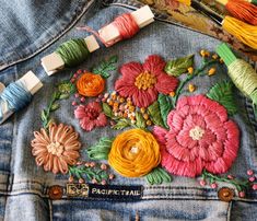 embroidered flowers and leaves on the back of a jean jacket with thread spools