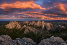 the sun is setting over some rocks and trees in the distance, with pink clouds above them