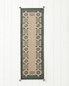 a rug hanging on the side of a wall next to a wooden floor and white walls