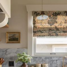 a kitchen with marble counter tops and an island in front of a window that has roman shades on the windowsill