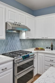 a kitchen with white cabinets and marble counter tops, stainless steel oven hoods and an island