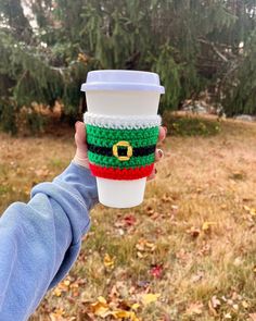 a person holding up a coffee cup in their hand with a crocheted christmas hat on it