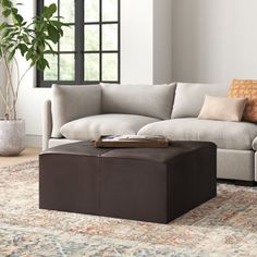 a living room with a couch, ottoman and coffee table in front of a window