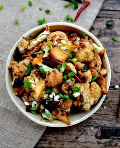 a white bowl filled with food sitting on top of a wooden table next to green onions