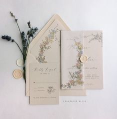 the wedding stationery is laid out on top of each other, with flowers and foliage