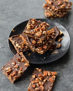 several pieces of chocolate pecan bars on a black plate with chopped pecans in the background