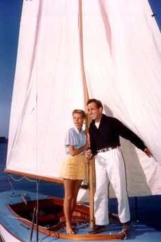 a man and woman standing on the front of a sailboat